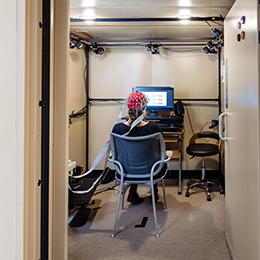 Image of a person sitting in front of a monitor with their bake towards the camera getting a EEG brain scan 400 square.